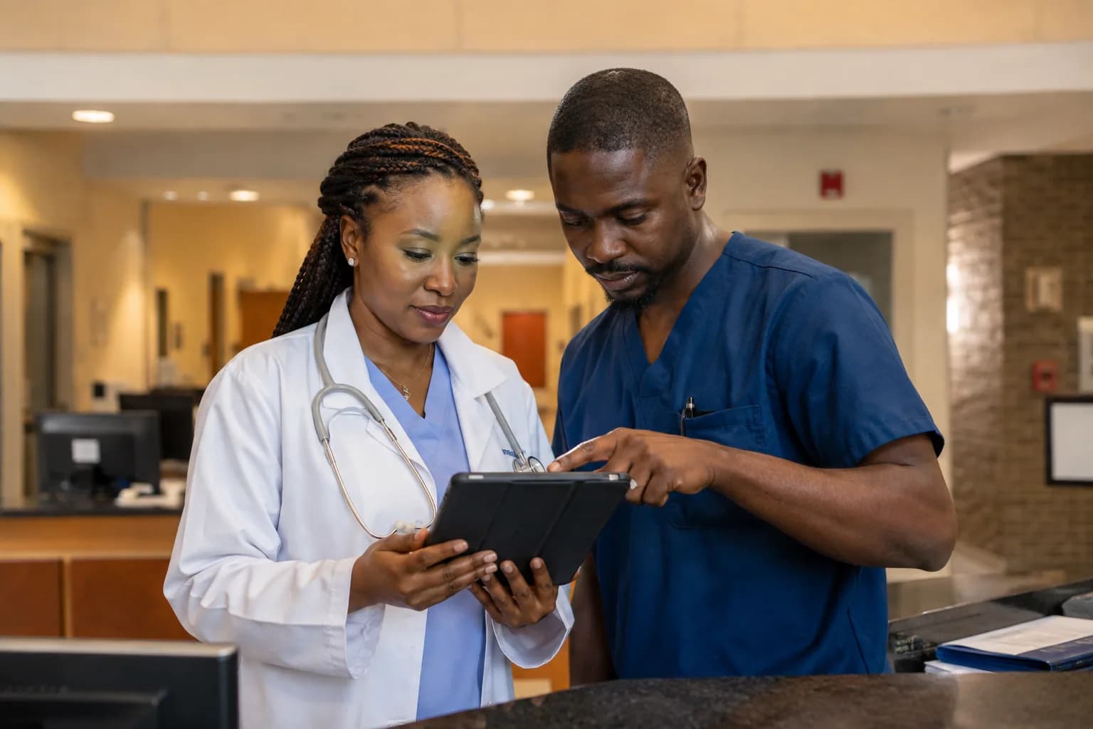 A doctor and nurse reviewing a tablet at a hospital station